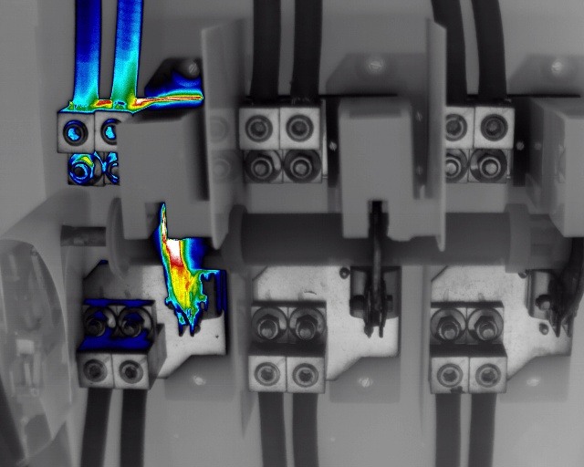 Thermal image overlay of an industrial electrical busbar inside a power distribution panel, highlighting a hotspot at one lug termination caused by localized overheating from a degrading electrical connection. 