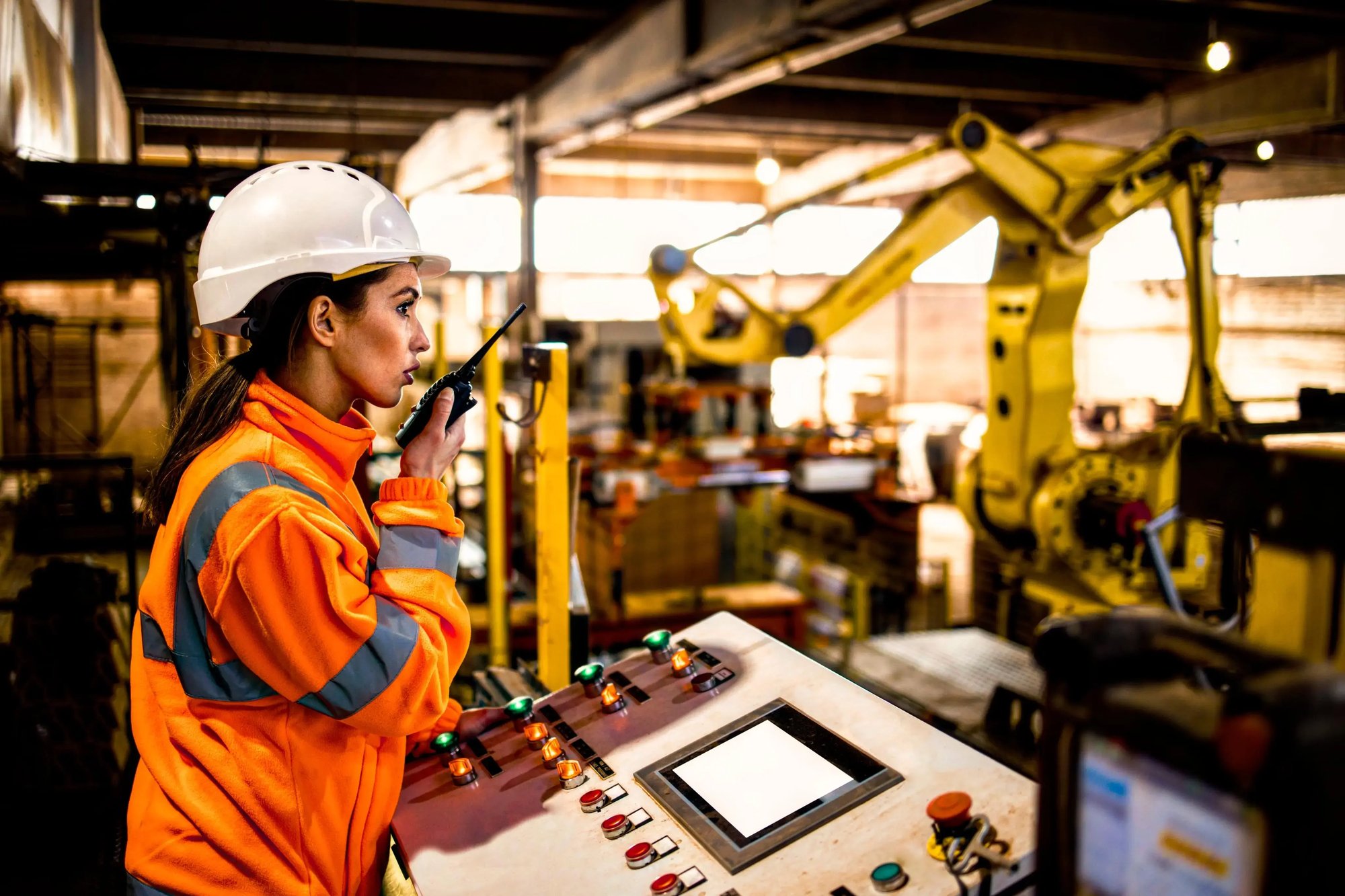 Technician in a hard hat and hi-vis vest speaking on a radio in a distribution facility.